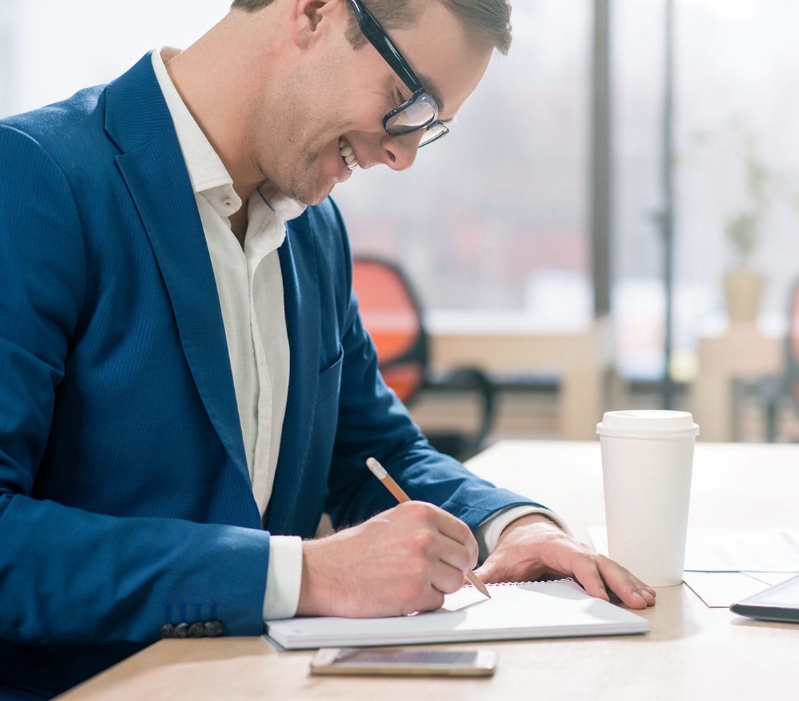 Un homme en costume sourit en écrivant des notes sur un bloc-notes.